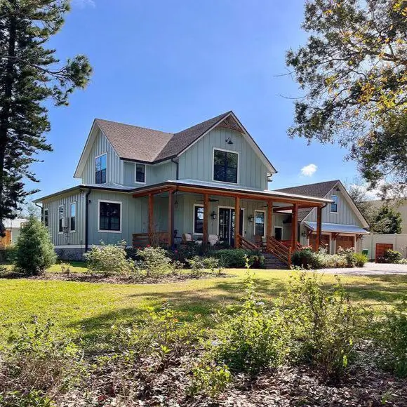A modern country house design with sage green siding and a large porch framed with natural wood beams.