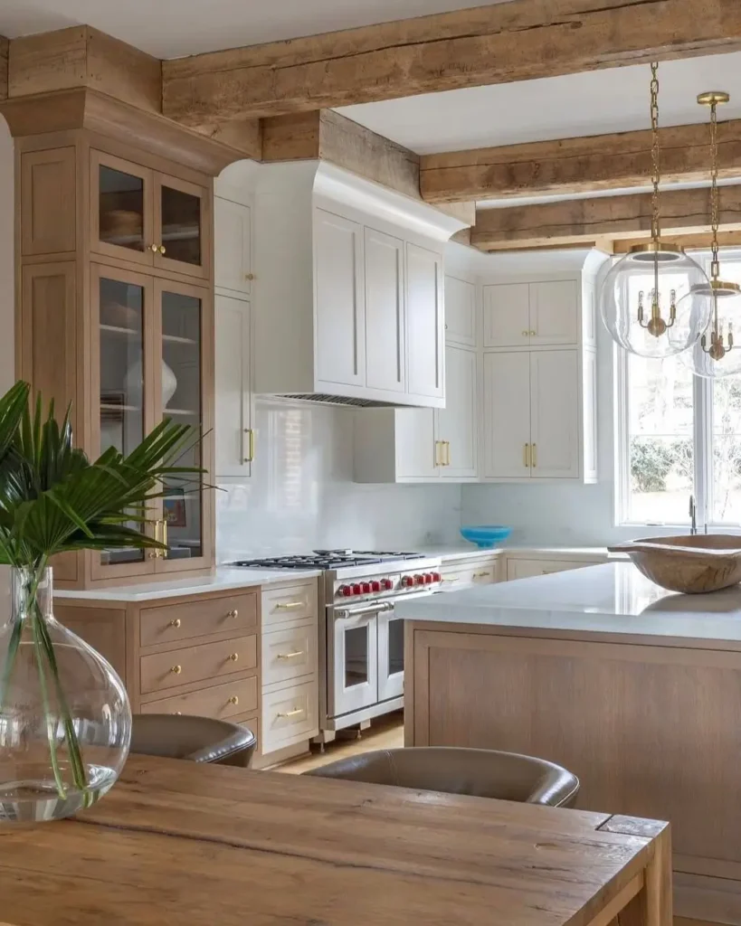 A refined rustic kitchen with two-tone cabinets in light wood and white, accented by exposed ceiling beams and gold hardware.
