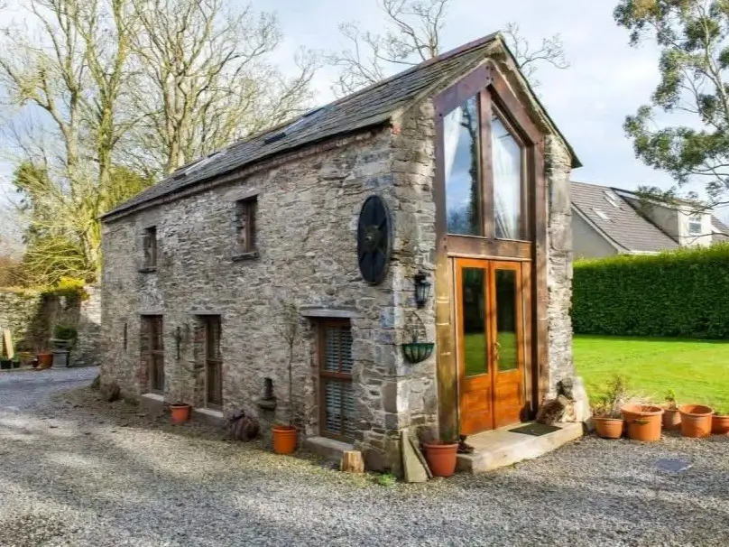 A rustic stone cottage converted into a modern home with a large glass A-frame entrance.