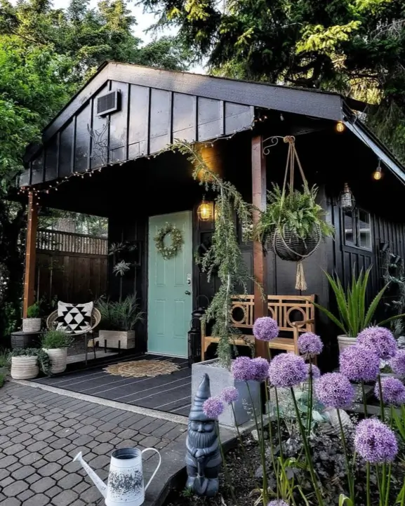A charming black garden shed with a colorful door, creating a cozy backdrop for lush plants and flowers.