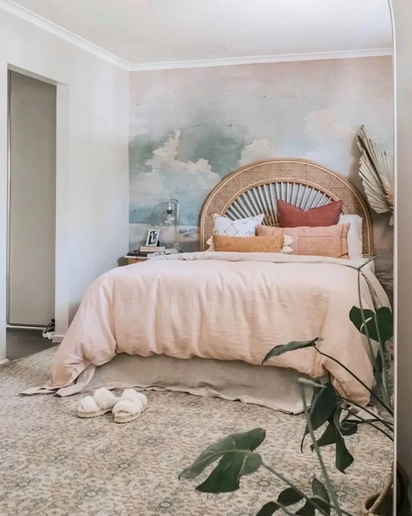 A boho bedroom featuring a soft watercolor cloud mural on the accent wall behind an arched rattan headboard.