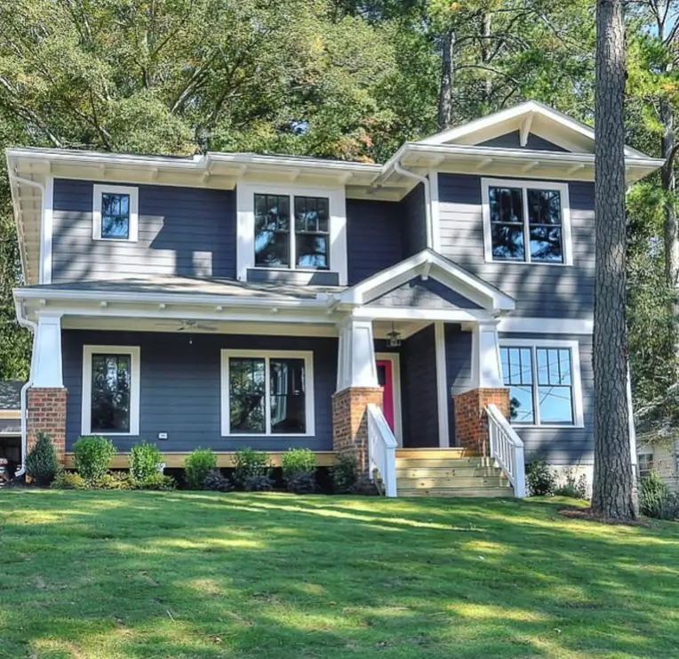 A modern craftsman house exterior with dark charcoal siding, white trim, brick porch piers, and a bright pink front door.