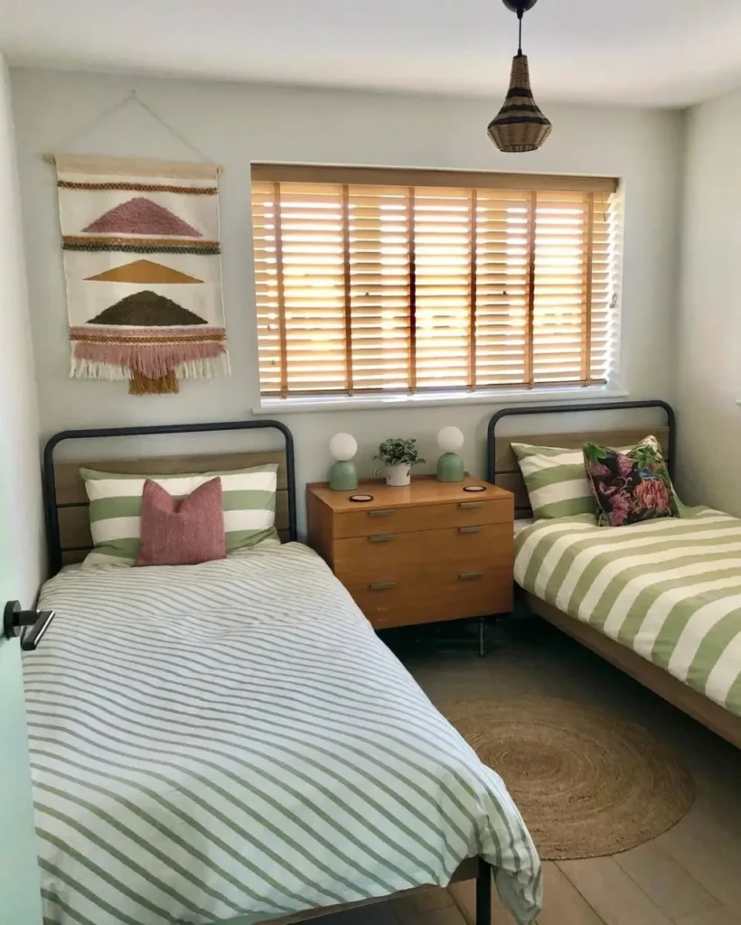 A small cozy bedroom idea for a shared space with two twin beds featuring green striped bedding and a central wooden dresser.