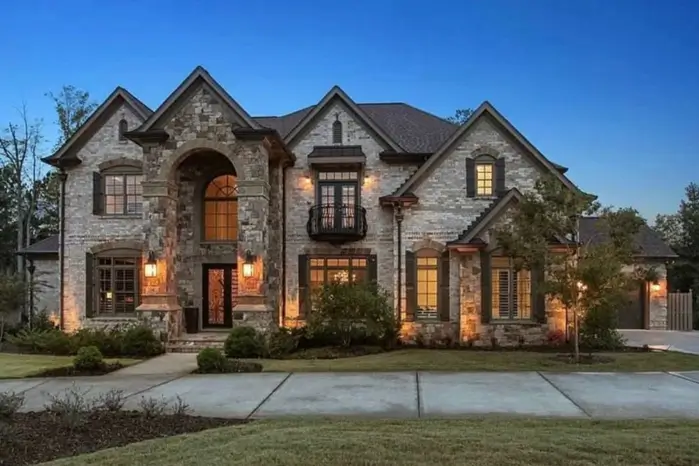20 Stone Mansion Ideas for Classic & Modern Designs 21 A stone mansion at dusk with warm exterior lights illuminating the textured stone facade and a grand arched entryway.