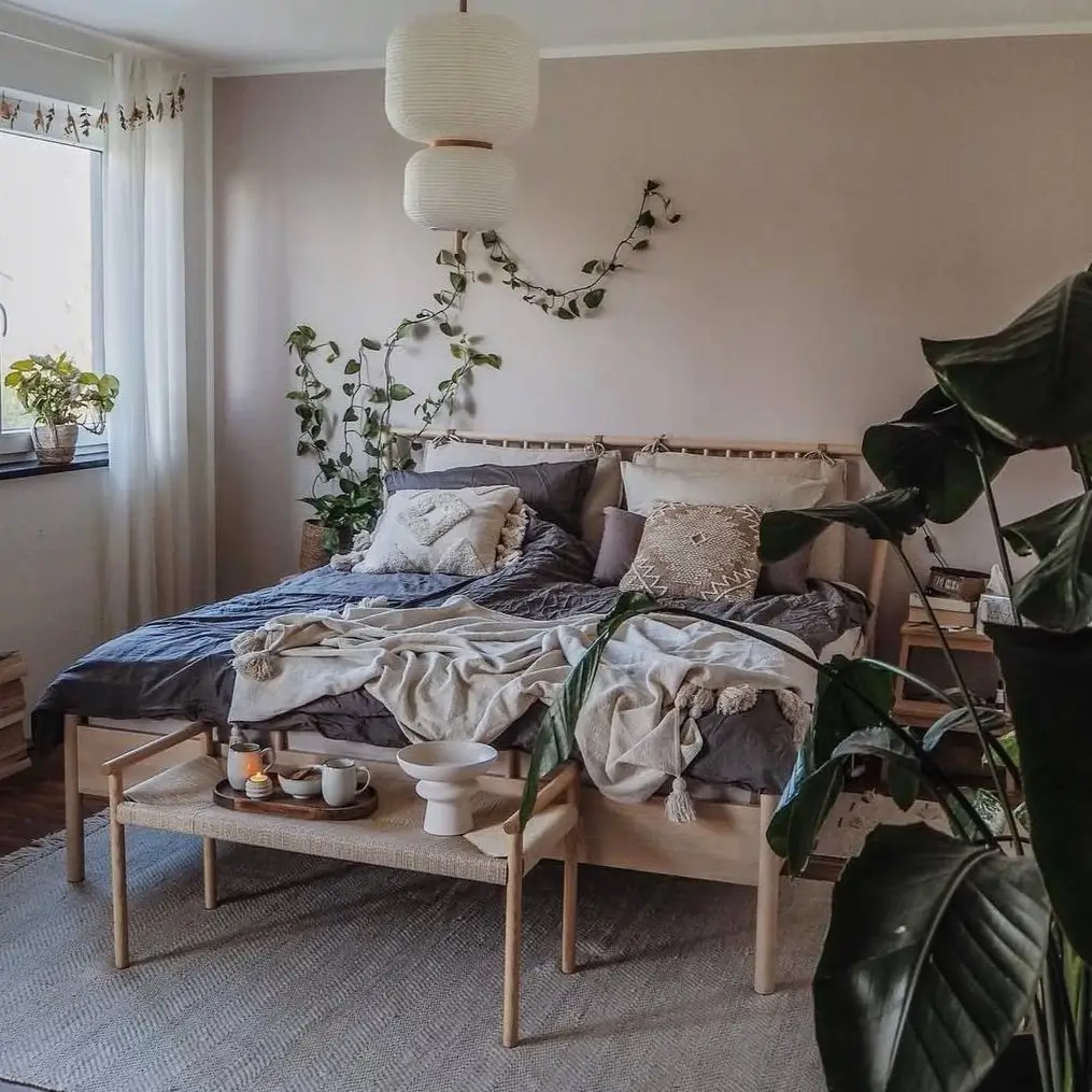 A cozy bedroom with dusty rose walls, a light wood bed with layered gray and cream bedding, and paper lanterns.