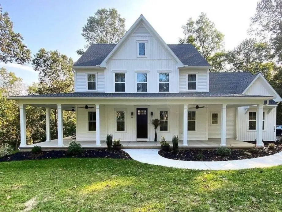 A large off-white farmhouse with a wraparound porch and a modern curved white walkway leading to a black front door.
