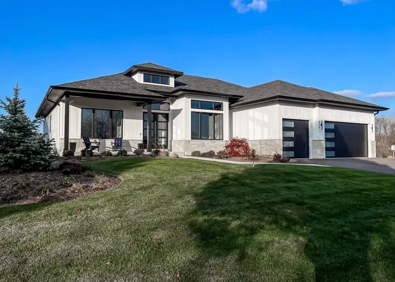 A contemporary white ranch style house with black trim, a stone accent wall, and a two-car garage.
