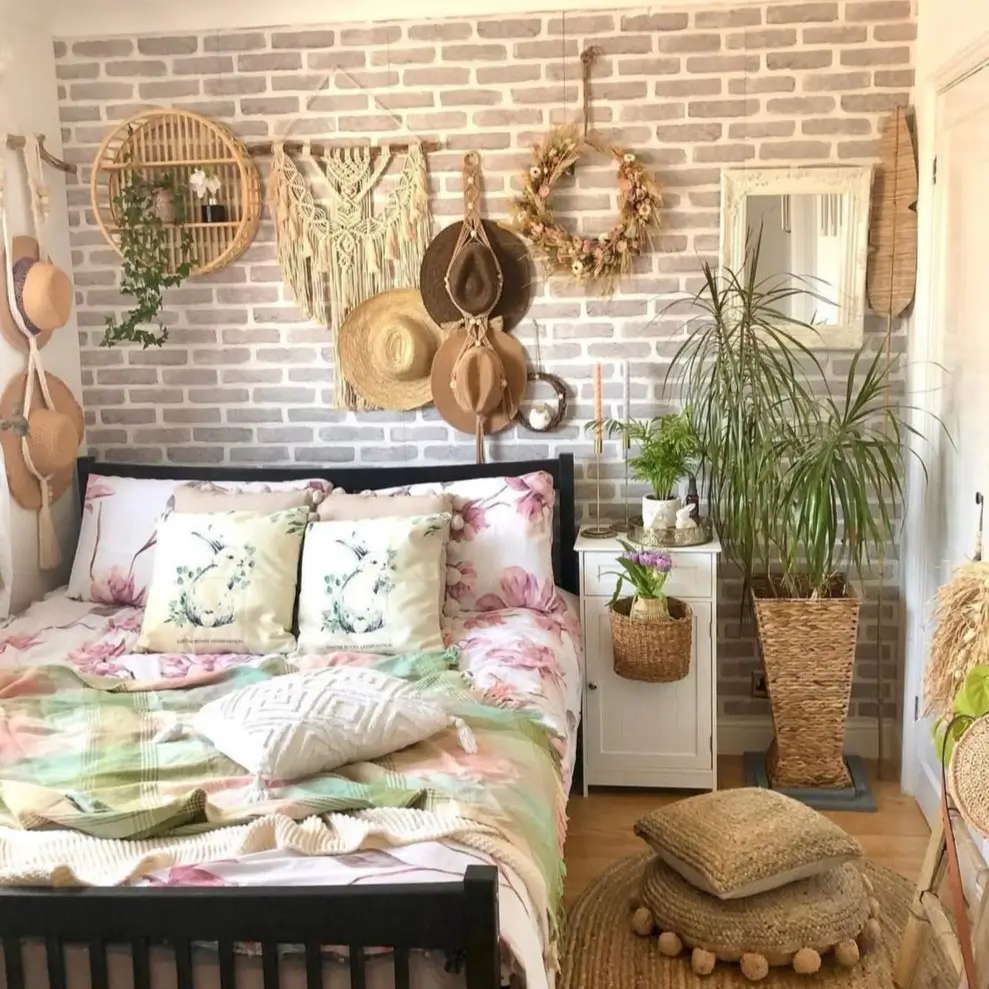 An eclectic bedroom with a gray faux brick wall, decorated with macrame, straw hats, and floral bedding.