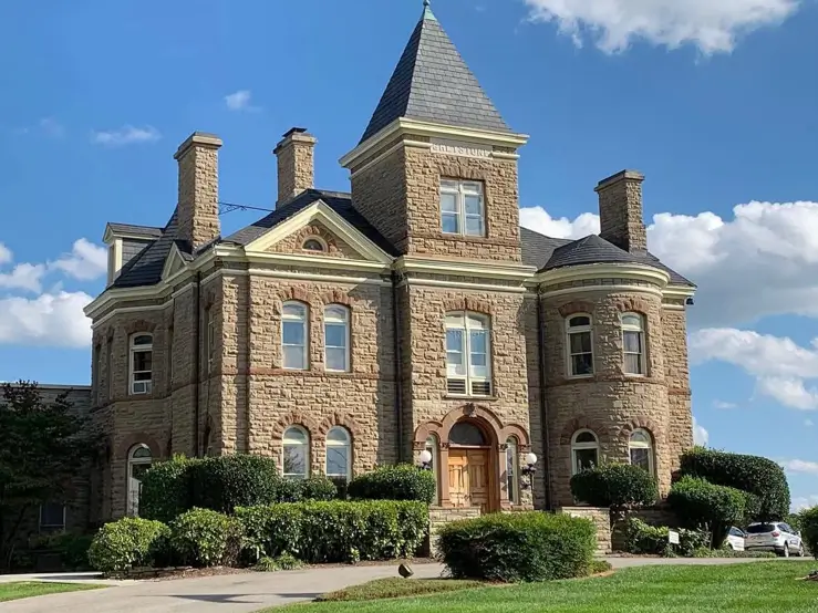 20 Stone Mansion Ideas for Classic & Modern Designs 4 A grand stone mansion under a bright blue sky, showcasing a central turret, multiple chimneys, and a rounded stone bay.