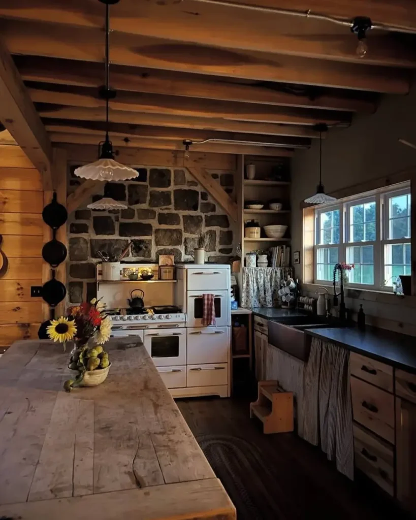 A simple rustic kitchen with a prominent stone wall, exposed wood ceiling beams, and a large wooden farmhouse table.