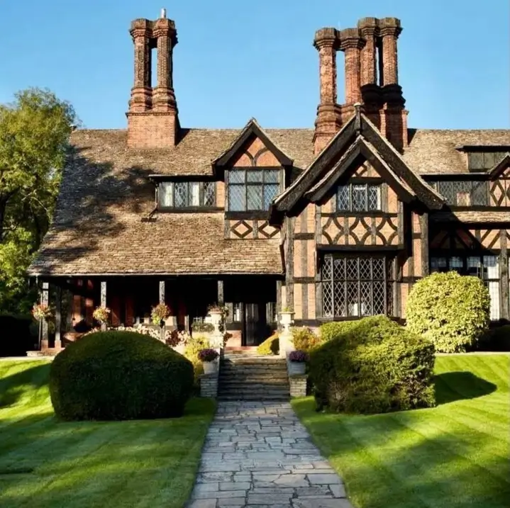 Grand Tudor-style British country house with characteristic half-timbering and elaborate chimney stacks.