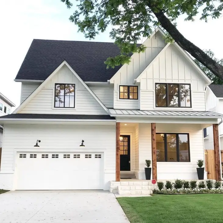 An inviting white modern farmhouse with natural wood beams supporting the porch and a manicured front lawn.