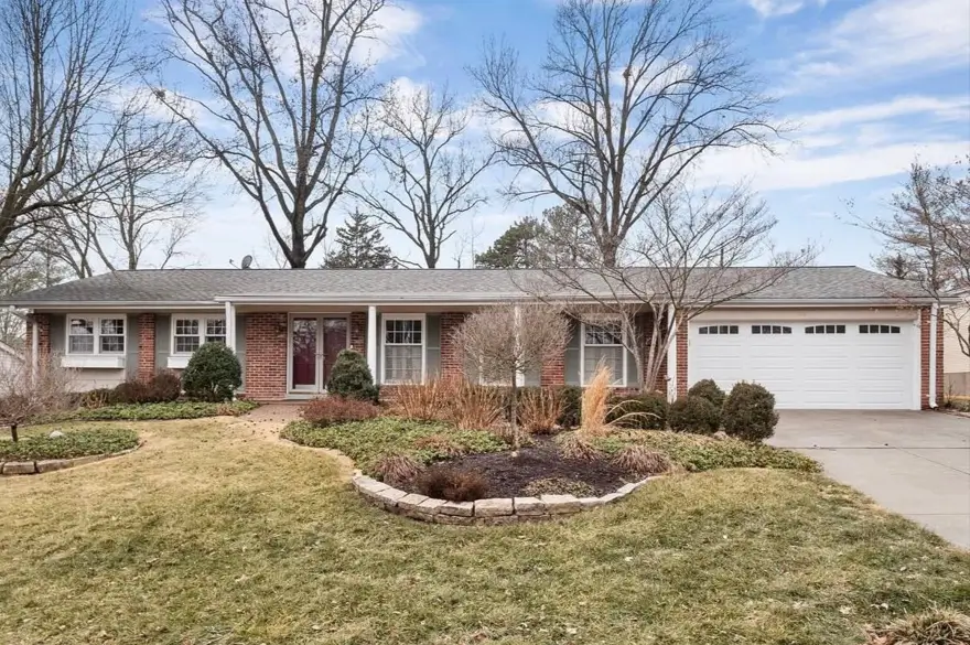 A sprawling brick mid-century ranch house with curved garden beds and mature trees.