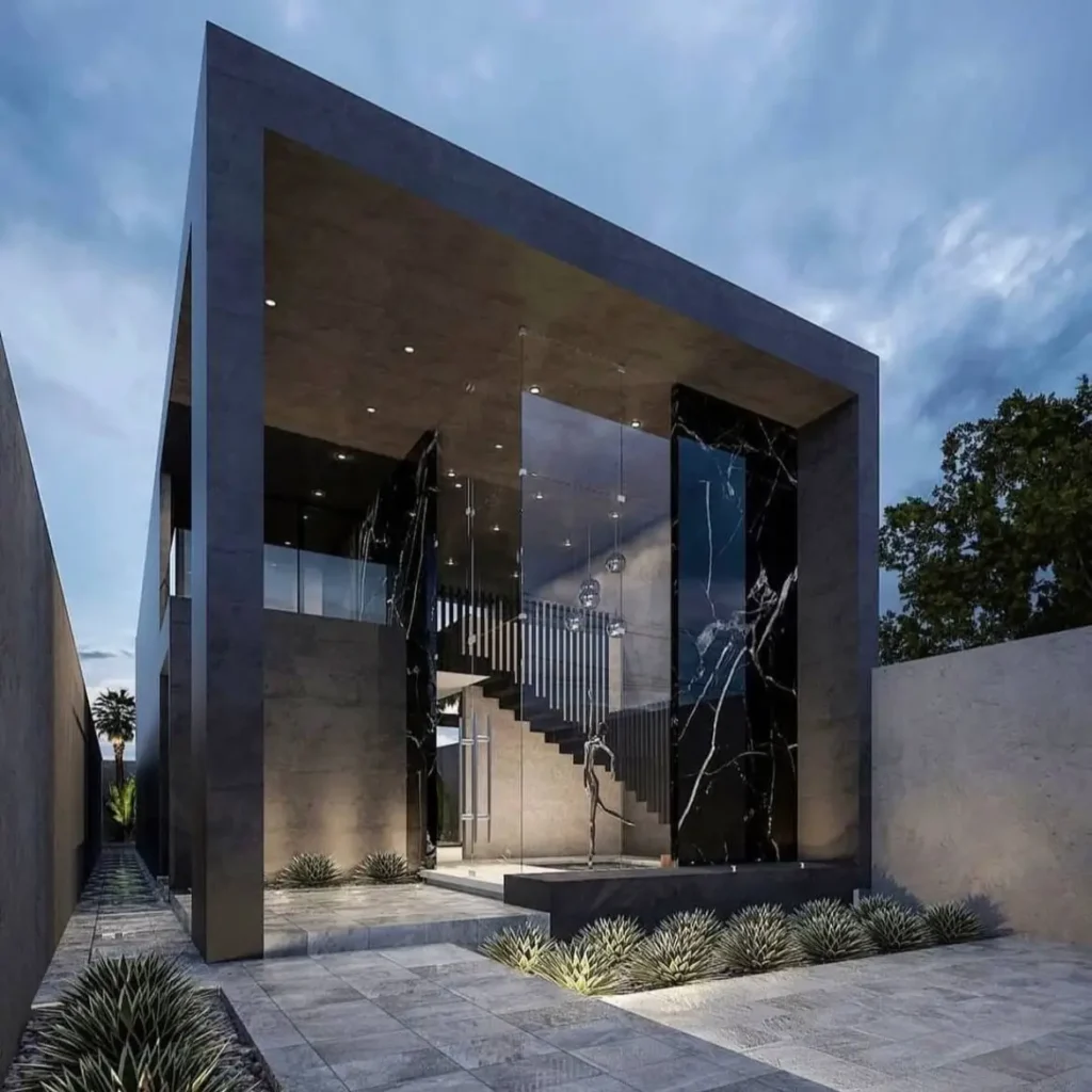 A contemporary concrete home featuring a dramatic glass entryway that reveals a polished black marble wall.