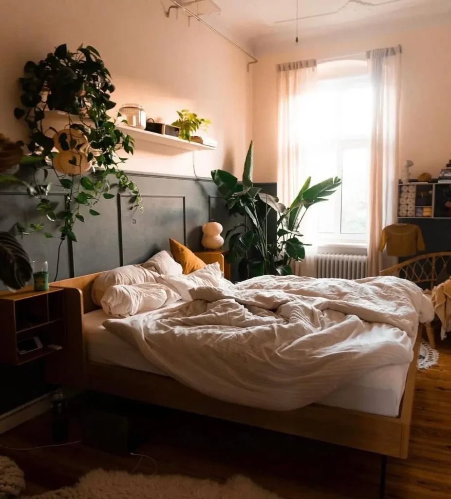 A cozy bedroom with a dark gray paneled wall behind a wooden bed with soft, messy white bedding.