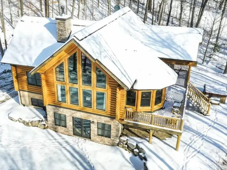 Embracing Grandeur: 25 Inspiring Ideas for Large Log Cabin Homes 23 An aerial view of a large log cabin in the snow, featuring a stone walkout basement and a sunlit wall of windows.