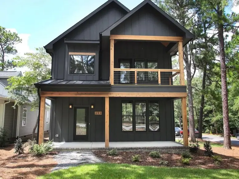 A two-story modern black house with natural wood framing defining the outdoor porch and balcony spaces.