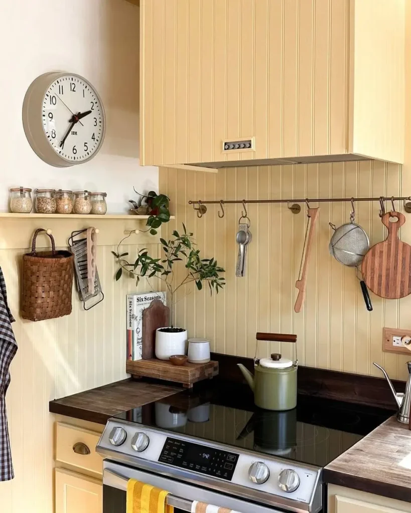 A simple rustic kitchen with sunny yellow beadboard cabinets, dark wood countertops, and a hanging utensil rack.
