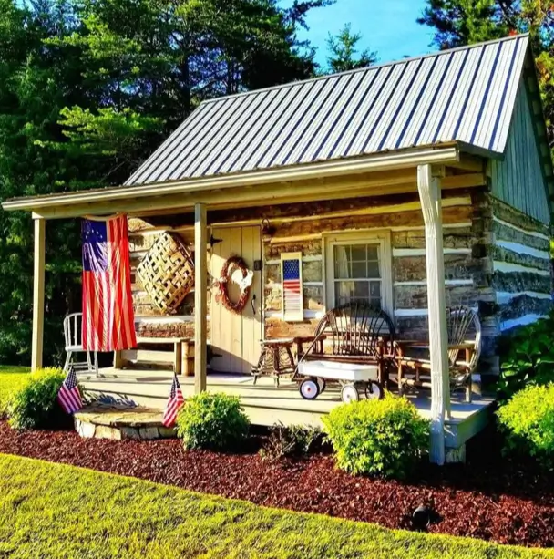 Small Log Cabins: 36 Ideas for Cozy Living & Enduring Charm 23 A small rustic log cabin with a decorated front porch, rocking chairs, and a metal roof.