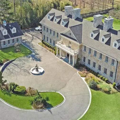 20 Stone Mansion Ideas for Classic & Modern Designs 22 An aerial view of a large stone mansion and matching guest house, connected by a circular driveway with a central water feature.