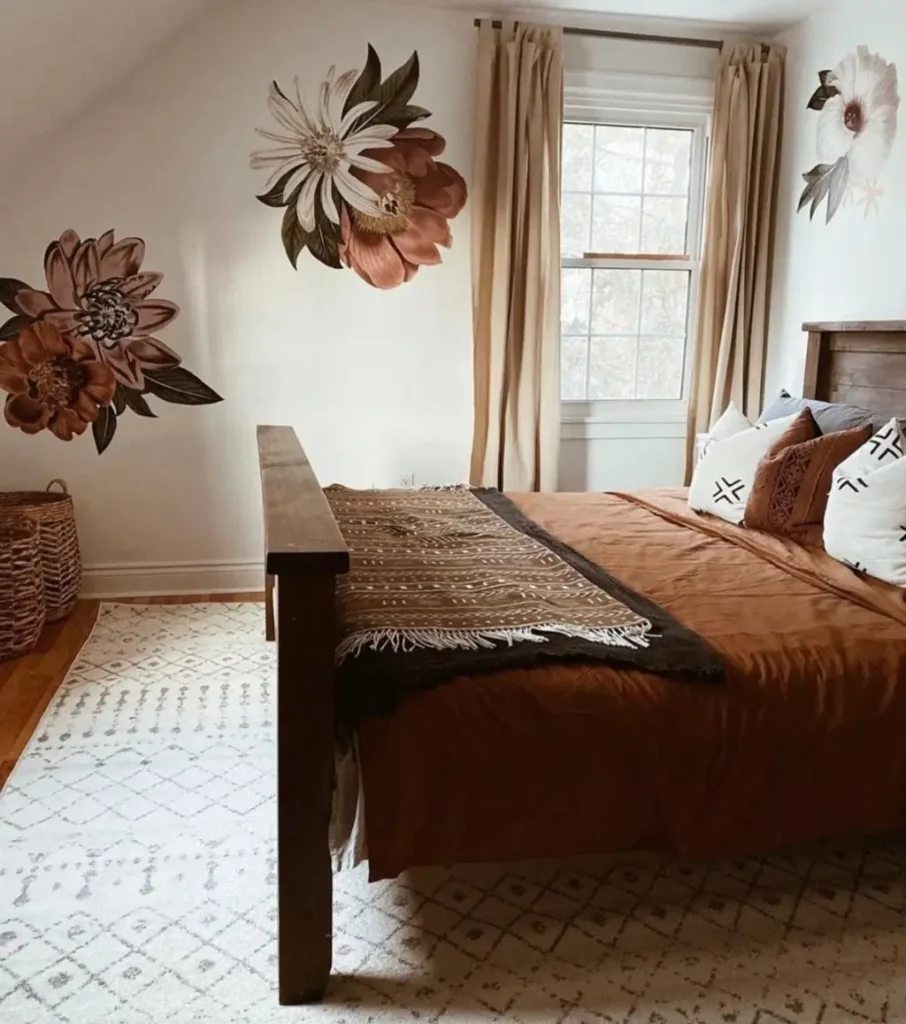 A cozy boho bedroom with large, artistic floral decals on the walls around a dark wood bed with rust-colored bedding.