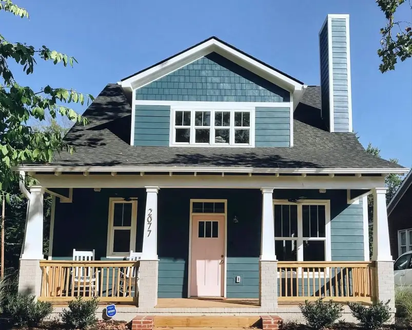 A deep teal craftsman house exterior with a full-width porch, white columns, and a soft pink front door.