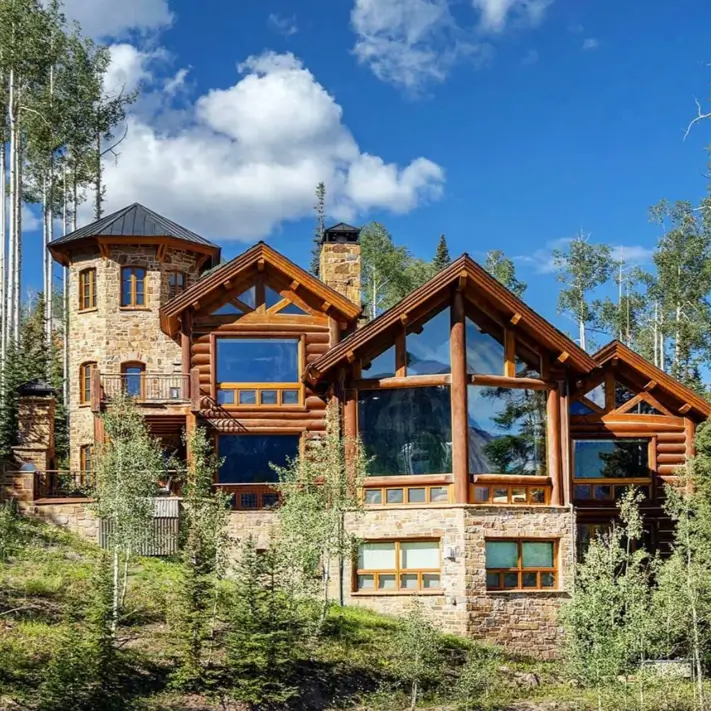 Embracing Grandeur: 25 Inspiring Ideas for Large Log Cabin Homes 24 A large log cabin home with a prominent stone turret and foundation, viewed from a low angle against a blue sky.