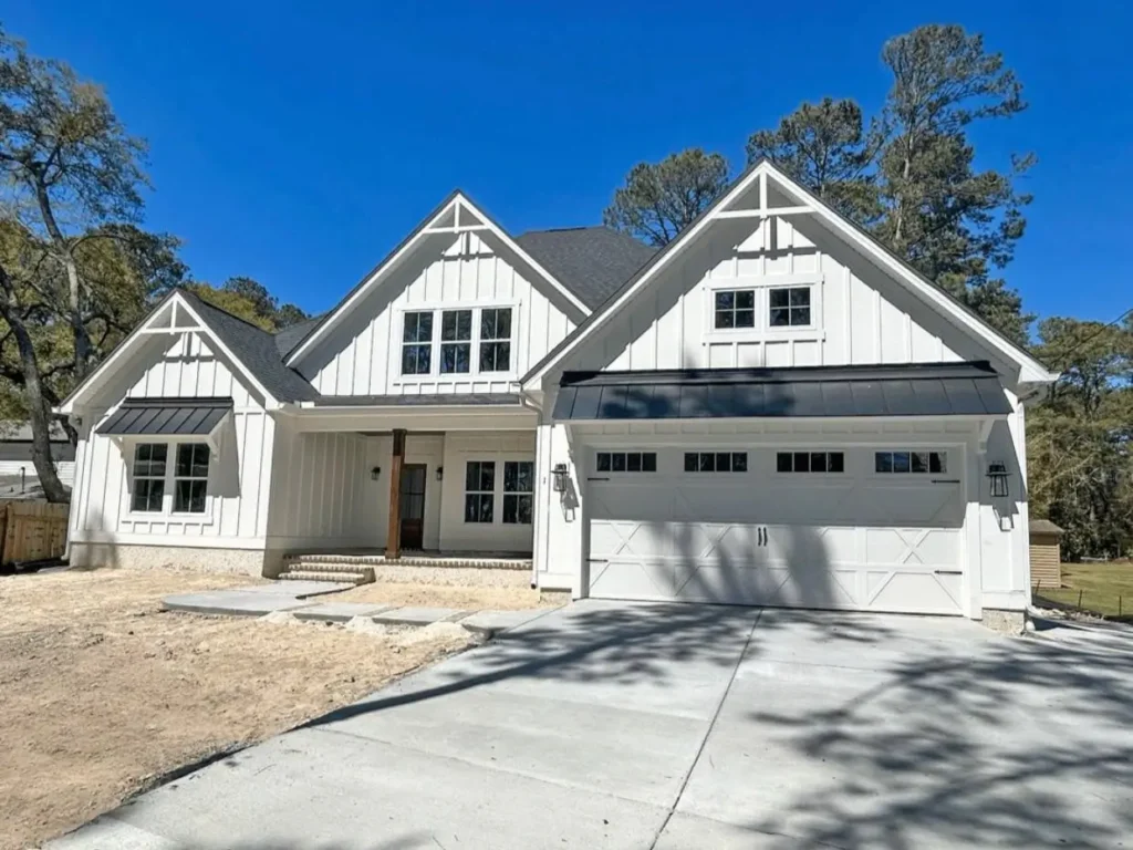 A modern off-white farmhouse with decorative trim in the gables and black metal roofs.