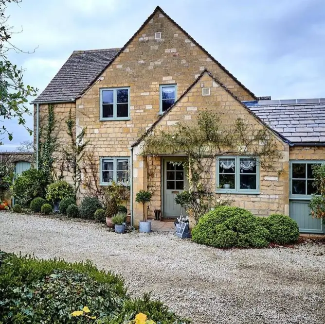 A stone British country house with sage green window trim and a gravel driveway.