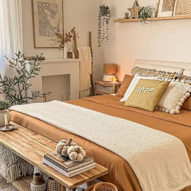 A warm and cozy bedroom with terracotta-colored bedding, a cream sherpa throw, and a wooden bench at the foot of the bed.