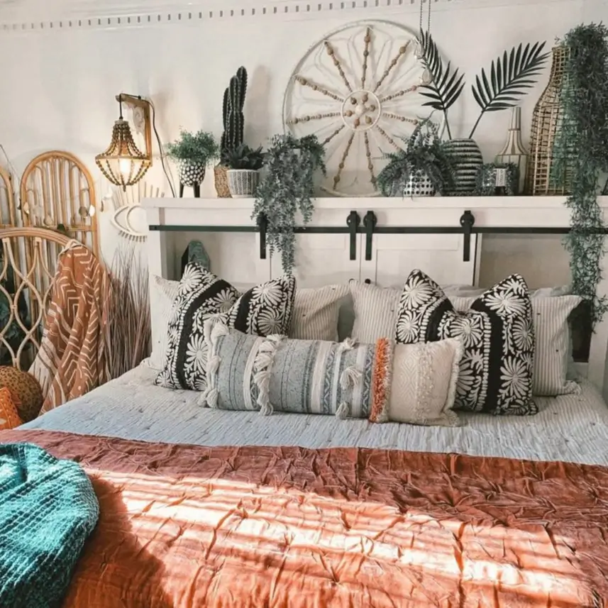 A white headboard shelf styled with an array of potted plants, palm fronds, and a decorative shell wheel, creating a lush boho bedroom look.