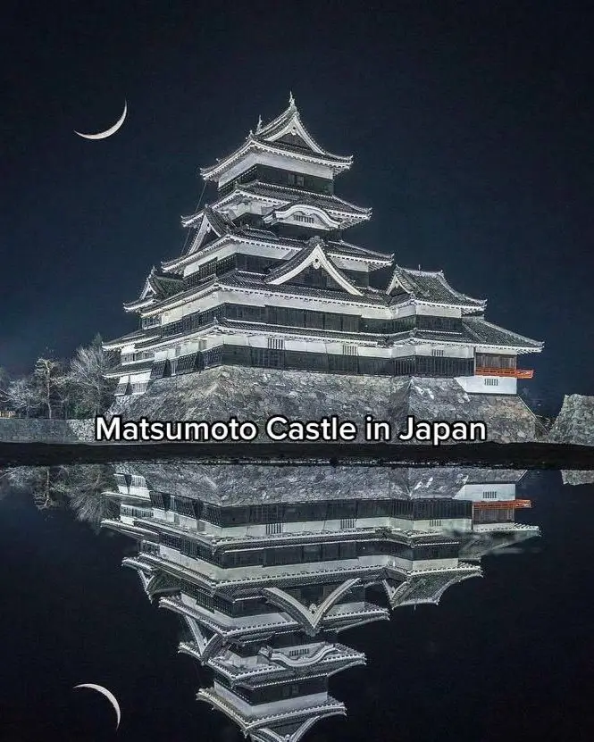 A traditional Japanese castle with tiered pagoda-style roofs reflecting perfectly in the water at night.