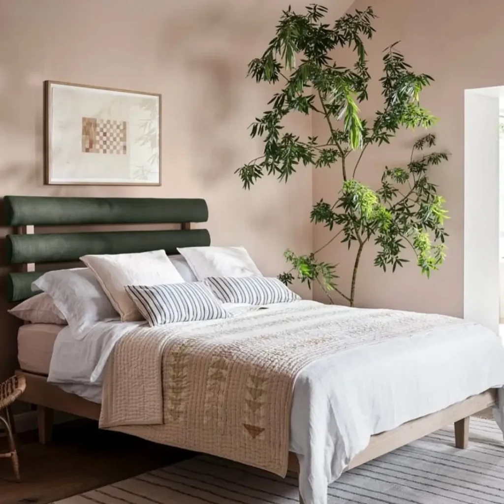 A bedroom with dusty pink walls, a dark green channel-tufted headboard, and light-colored bedding.