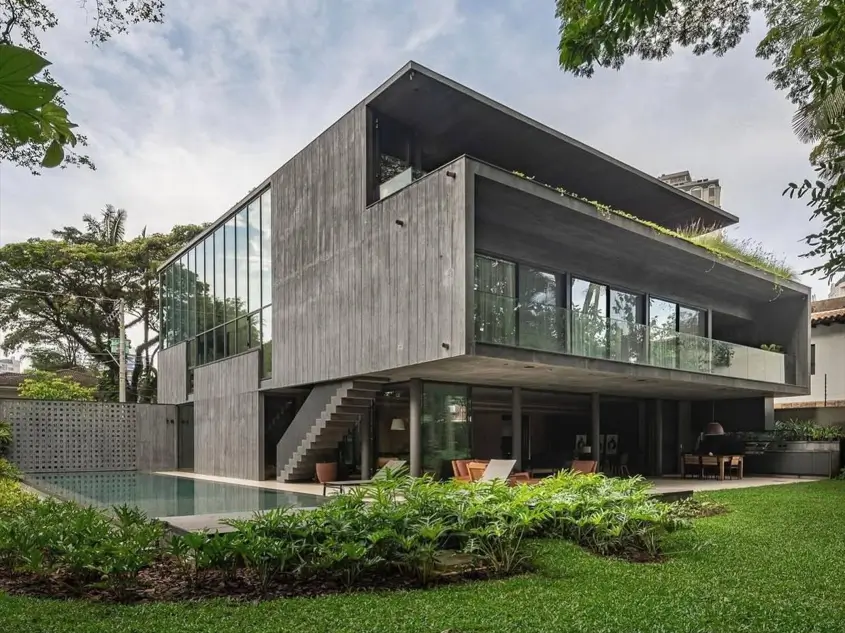 A large contemporary concrete home with board-formed texture, a poolside patio, and extensive glass walls.
