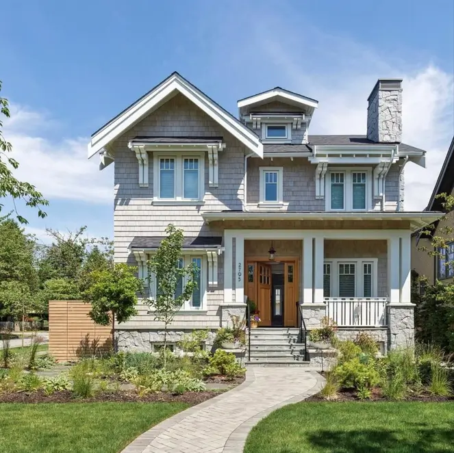 A light beige shingle craftsman house exterior featuring a natural stone foundation, porch columns, and a large stone chimney.