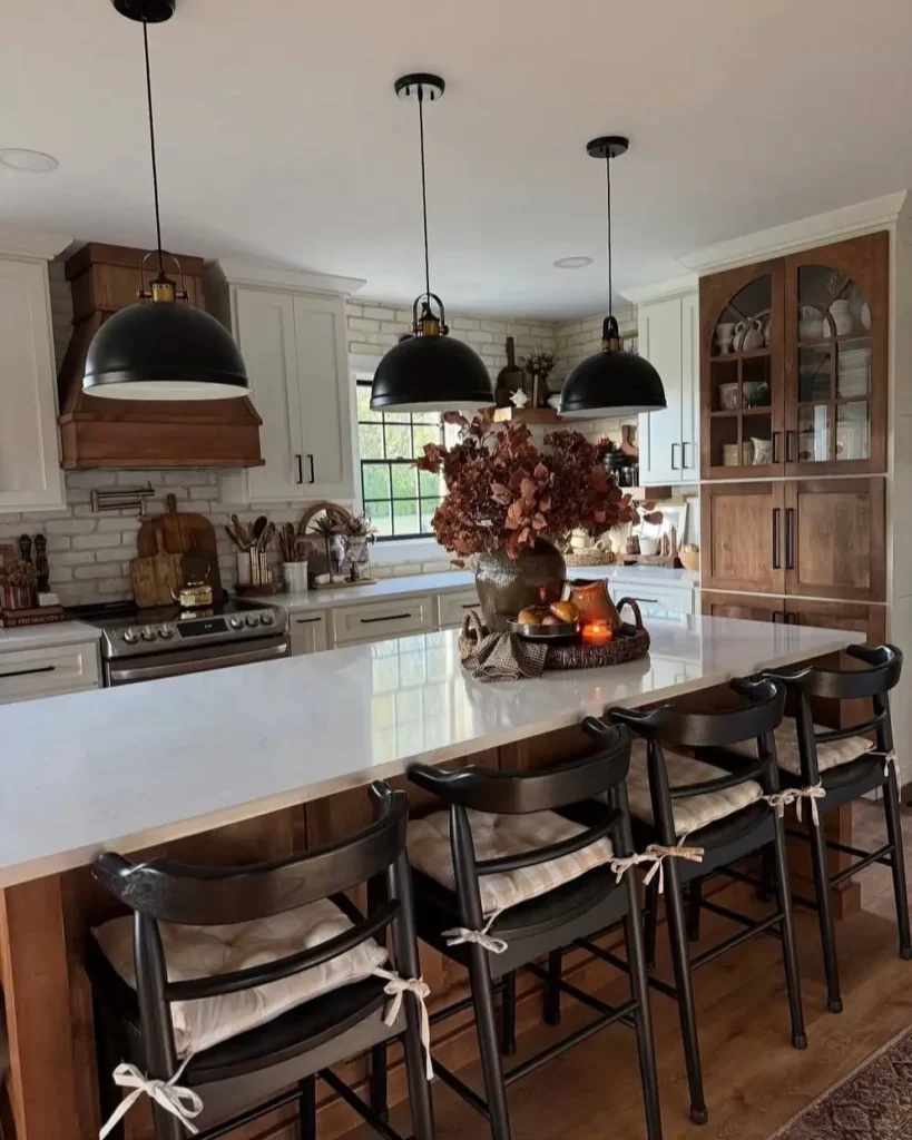 A rustic kitchen with a whitewashed exposed brick wall, a large white island, and black metal dome pendant lights.