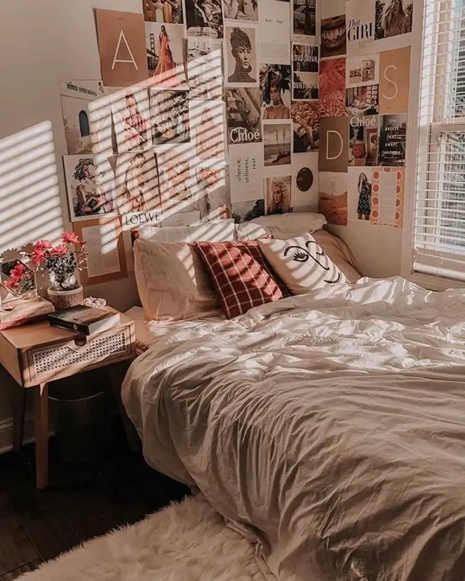 A small cozy bedroom with a large collage wall of pictures behind a bed with white linens, illuminated by morning sunlight.
