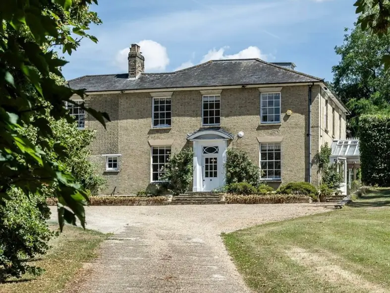 A stately British country house with a light brick exterior and a classic gravel driveway leading to the front door.