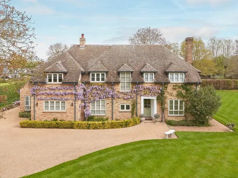 A large brick British country house with beautiful purple wisteria climbing across the front.