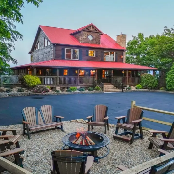 Embracing Grandeur: 25 Inspiring Ideas for Large Log Cabin Homes 27 A large cabin-style home with dark siding, a vibrant red metal roof, and a gravel fire pit area in the foreground.