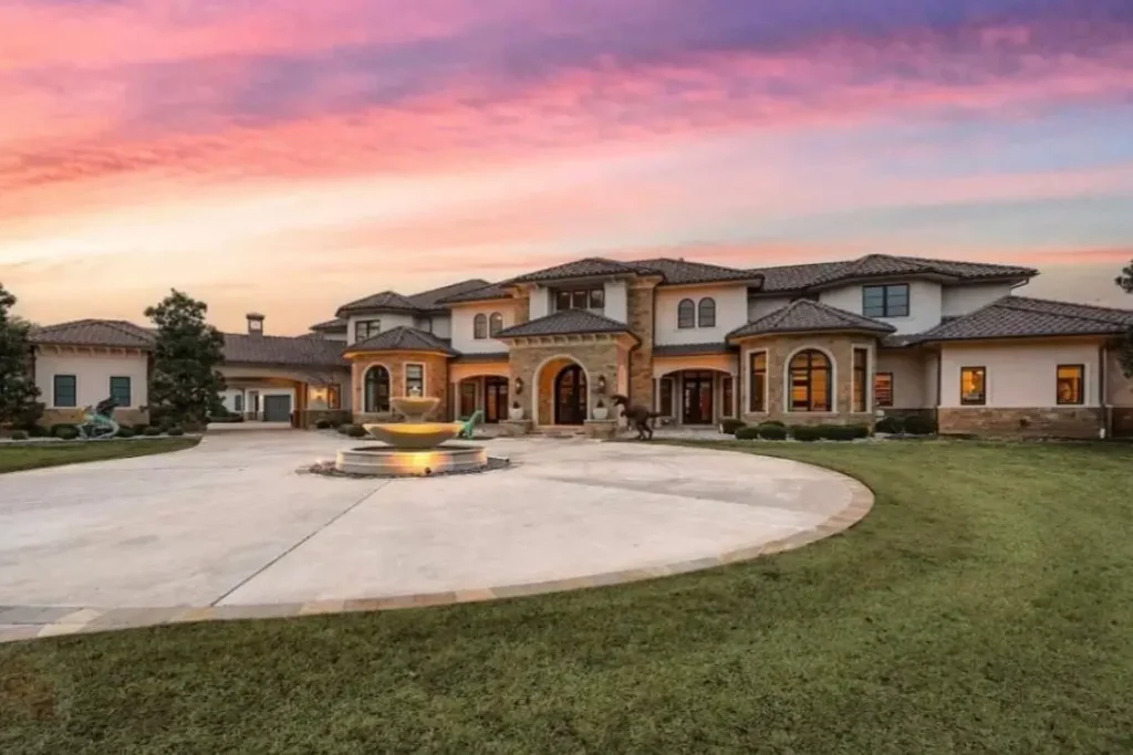 The Ultimate Guide to Luxury Mansion Design: 33 Ideas for Grandeur 27 A modern luxury mansion with a sculptural fountain in the driveway against a pink sunset.
