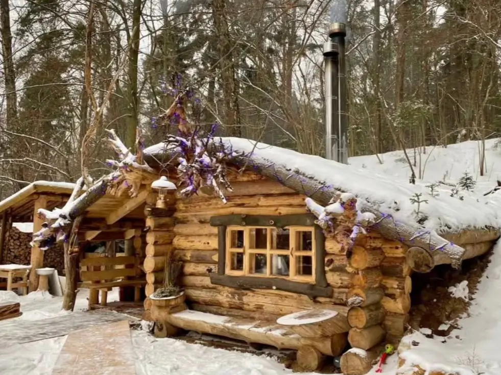 60 Charming Small Log Cabin Ideas to Inspire Your Rustic Retreat 26 A rustic small log cabin built into a snowy hillside with a prominent metal chimney pipe.