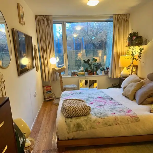 A cozy bedroom at dusk with warm lamps illuminated, featuring a wooden bed with a chunky knit blanket.