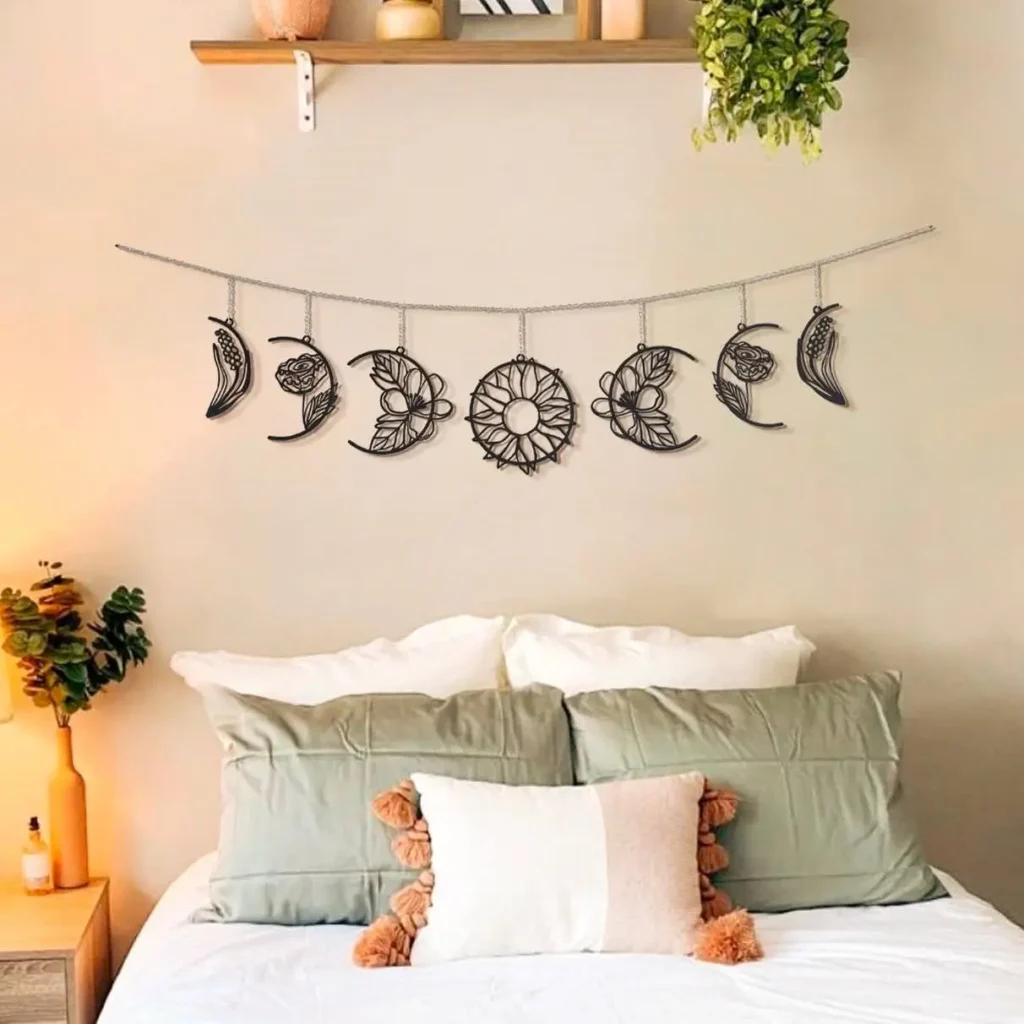 A black metal moon phase garland hanging on a beige wall above a bed with sage green and white pillows.