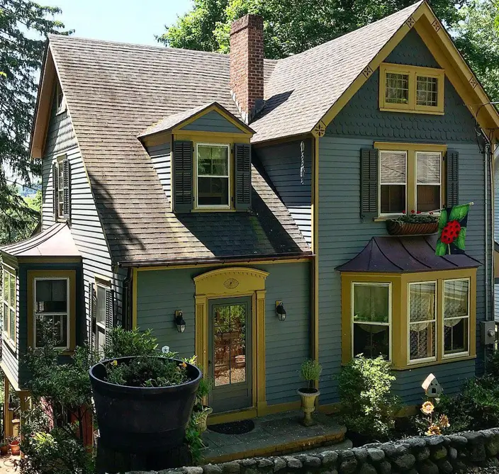 A unique country house design with slate blue siding, distinctive golden ochre trim, and charming bay windows.