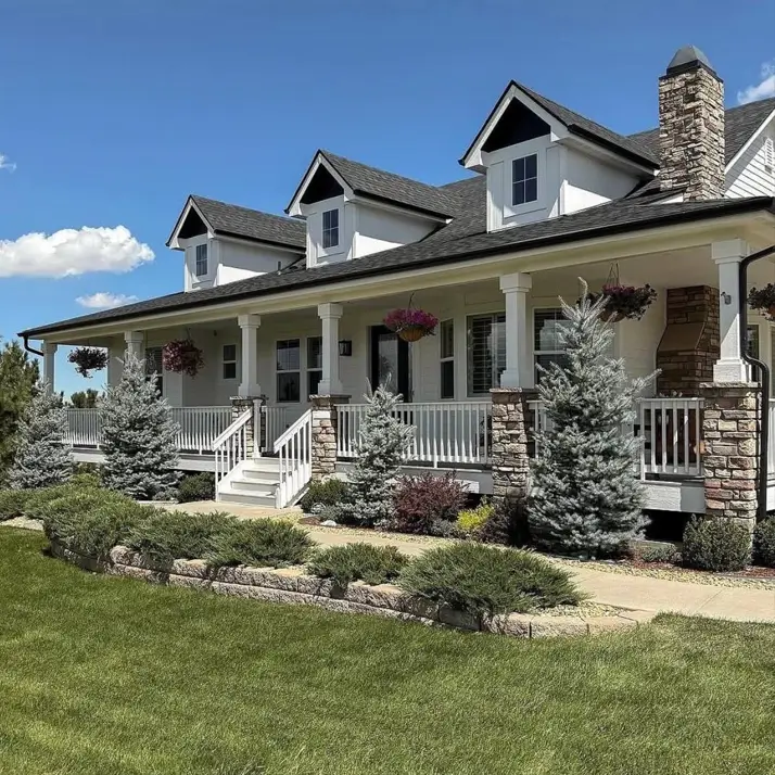 A classic off-white farmhouse with a large porch supported by stone columns and a prominent stone chimney.