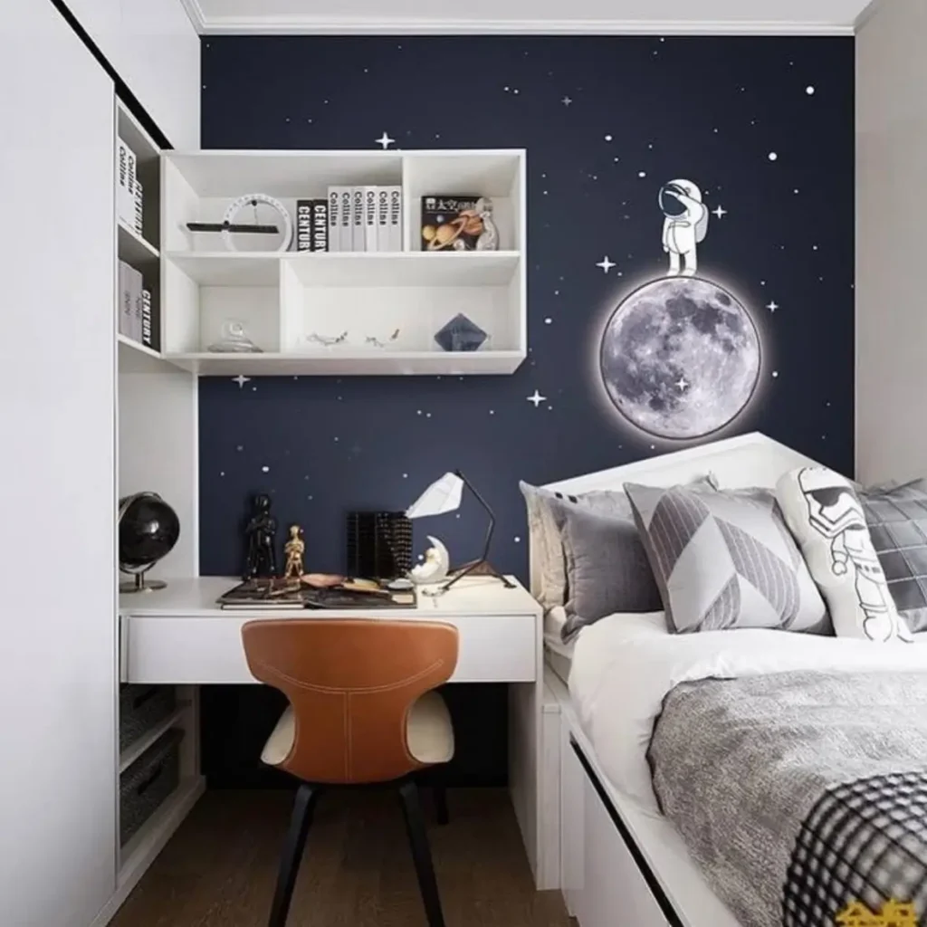 A small bedroom interior design with a space-themed accent wall featuring an astronaut on the moon above the bed and a built-in white desk.