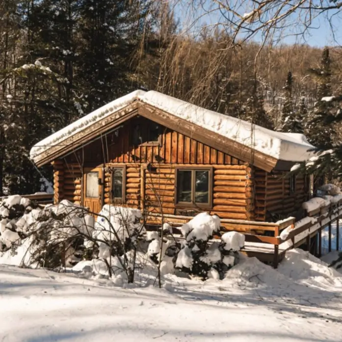 60 Charming Small Log Cabin Ideas to Inspire Your Rustic Retreat 27 A small log cabin in the sun, covered in deep snow, with a large overhanging roof in a forest setting.