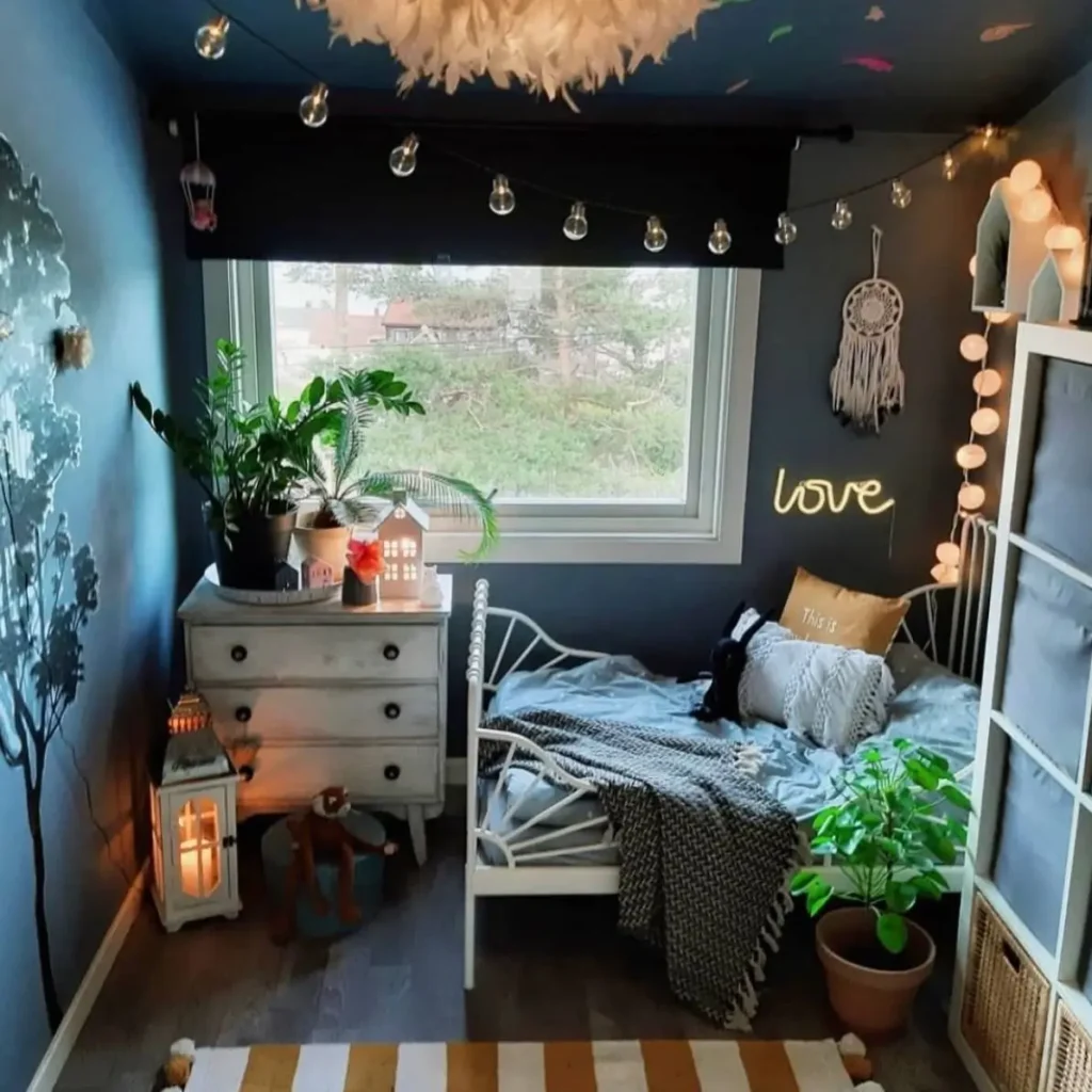 A cozy bedroom with dark blue walls, featuring a neon "love" sign, a dreamcatcher, and string lights hanging near the bed.