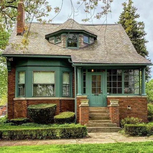A unique country house design with a brick base, deep teal trim, and a charming octagonal dormer window.